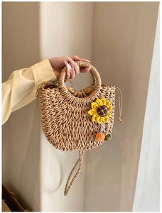 Close-up of woven straw handbag featuring sunflower decor and colorful pom-poms