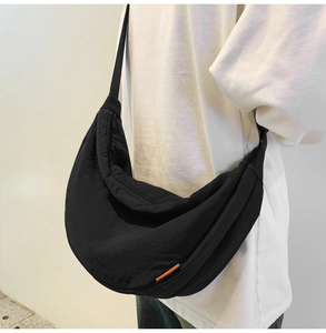 Detailed view of a black crescent nylon crossbody bag with an orange side tag on a model