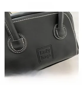 Close-up of white contrast stitching and lady bags embossed logo on black PU leather handbag
