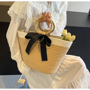 Detail of hand-woven straw bag with elegant black satin bow and round handles