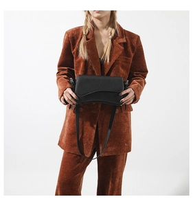 Close-up of black lychee-grain saddle bag paired with a stylish brown corduroy suit