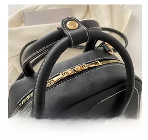 Detailed macro view of black Boston bag featuring white contrast stitching and gold hardware