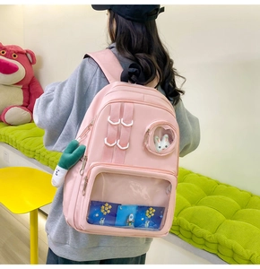 Detailed view of pink nylon backpack with clear window pocket and green plush charm