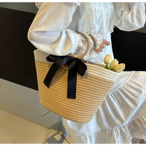 Close-up of woven tote bag featuring a black bow and natural wooden handle with tulips