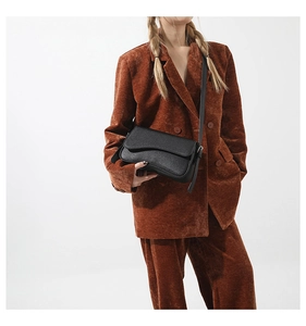 Detail of minimalist black pebbled leather crossbody bag on a brown corduroy suit