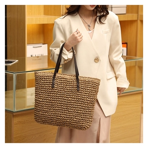 Detail view of woven straw tote bag with brown leather handles on casual chic outfit