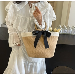 Detail of hand-woven straw tote bag with black ribbon bow and elegant round handle