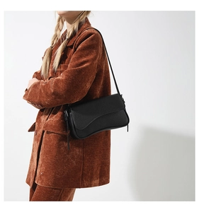 Detailed side view of a black pebble leather crossbody bag with a unique wavy flap edge