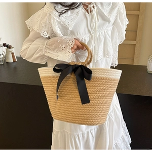 Detail of hand-woven rope tote bag featuring a large black satin bow and round handles