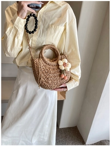 Detail of hand-woven straw bag with beige flower pendant and secure drawstring lining