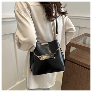 Détail d'un sac seau noir avec bandoulière chaîne dorée et texte Fashion jaune
