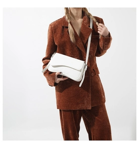 White textured leather crossbody bag styled with a brown suit in a studio setting