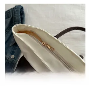 Détail de la fermeture éclair en métal doré et du tissu en nylon fin d'un sac cabas blanc