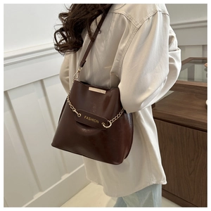 Sac seau marron avec détails de chaîne métallique et étiquette mode porté par un mannequin