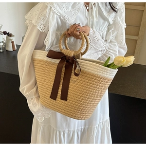 Macro shot of large straw tote bag with round handles and brown ribbon bow decoration