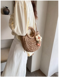 Fashionable straw shoulder bag with floral charm and drawstring lining on a model