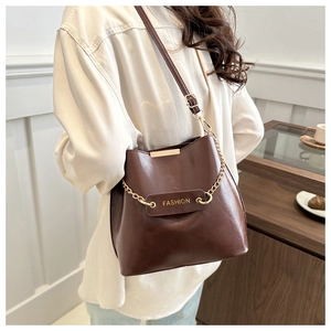 Sac seau en cuir marron avec chaîne dorée et logo tendance porté par un mannequin