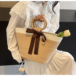 Detail of hand-woven straw bag with round handles and decorative brown satin bow