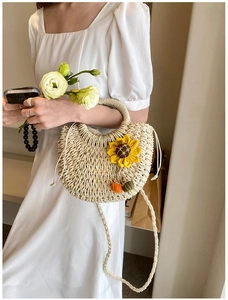 Dettaglio di una borsa in paglia intrecciata con decoro a girasole e ciondoli a pompon colorati