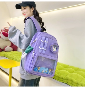Detail of purple nylon Ita bag with transparent PVC window and plush keychain on model