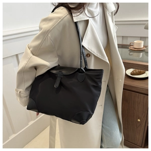 Détail d'un cabas minimaliste en nylon noir avec lanières en cuir sur un trench beige