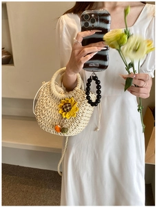 Close-up of woven straw handbag featuring a yellow sunflower and black beaded handle
