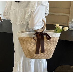Close-up of woven straw tote bag featuring a large dark brown silk bow and round handles
