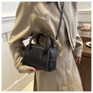Detail of black pebbled PU leather boston bag with white contrast stitching and gold hooks