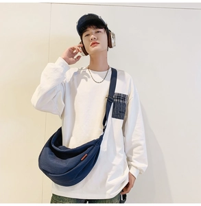 Detail of navy blue nylon crossbody bag featuring an adjustable strap and orange label accent