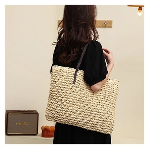 Detail of woven straw tote bag with brown leather strap worn by a model in home setting