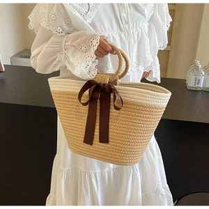 Detailed close-up of woven tote bag with a dark brown satin bow and round straw handles