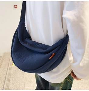 Detail of navy nylon crescent crossbody bag featuring an orange logo label and black strap
