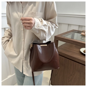 Détail d'un sac seau marron foncé brillant avec poutre dorée mate et bandoulière chaîne