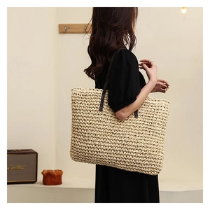 Close-up of the large woven straw tote bag featuring contrast dark leather handles