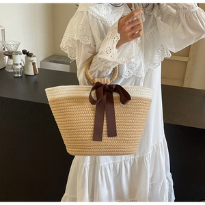 Detail of hand-woven straw handbag featuring a chic brown satin bow and round handles