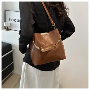 Détail d'un sac seau en PU marron avec chaîne dorée et étiquette Fashion sur un modèle