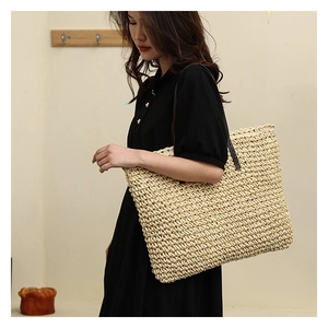 Close-up of woven straw tote bag with brown leather strap worn by a model