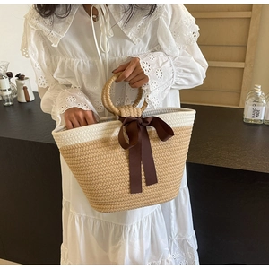 Detail of woven straw tote bag with brown ribbon bow and white crochet dress context