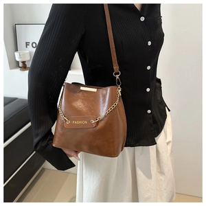 Détail du sac seau marron vintage avec chaîne dorée et écusson fashion sur cuir texturé