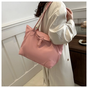 Détail d'un sac cabas en nylon rose porté avec un trench-coat dans un café