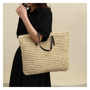 Close-up of woven straw tote bag texture and high-quality dark leather shoulder strap