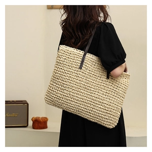 Detail of handwoven straw tote bag with brown leather strap in a casual lifestyle setting