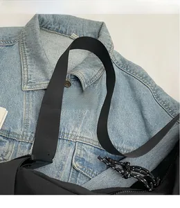 Detail of a black nylon crossbody bag featuring a smooth wide shoulder strap on denim