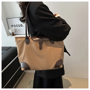Détail d'un sac cabas en nylon kaki avec finitions en cuir brun porté par un mannequin