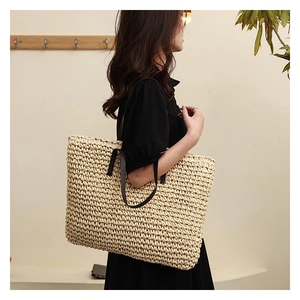 Detail of hand-woven straw tote bag with brown leather handles on shoulder of a woman