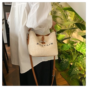 Detail showing the woven straw texture, brown leather trim, and horn buckle on the beige bag