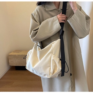 Detail of beige canvas crossbody bag with drawstring side pocket and black shoulder strap