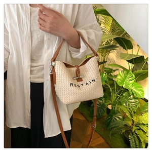 Détail du sac seau en paille tissée avec anses en cuir et logo brodé en noir