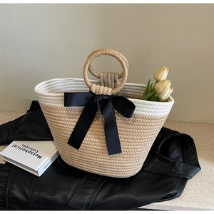 Minimalist woven handbag with black ribbon bow and elegant round handles in soft beige tone