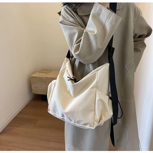 Minimalist beige canvas crossbody bag with wide black strap shown on a model